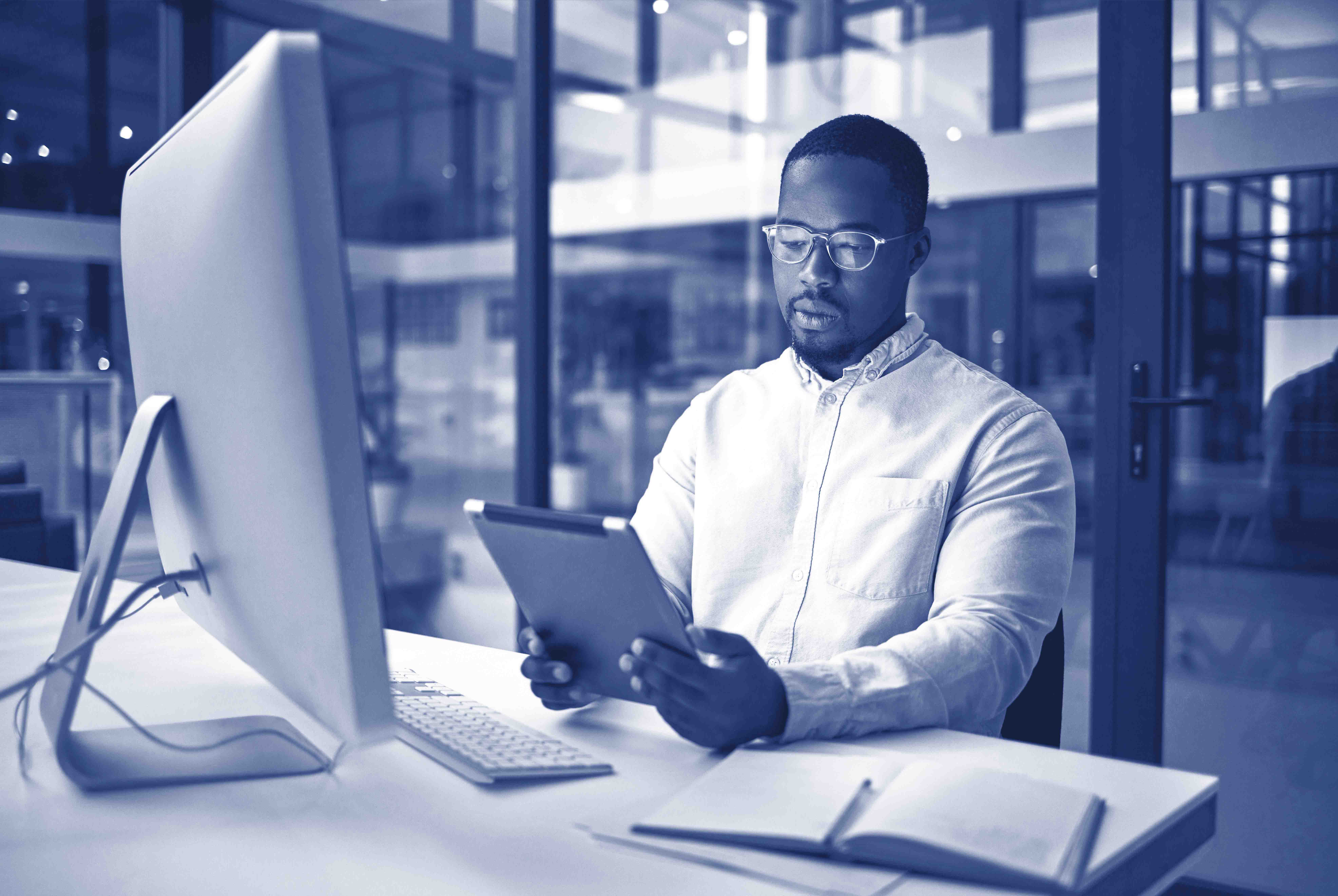 Black businessman, tablet planning and desktop at night in startup for online ideas, strategy and connect apps on 5g technology in Nigeria. Employee working in dark modern office for internet project